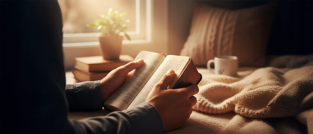 A close-up of a young person's hands (diverse, gender-neutral) holding a well-worn Bible, with light specifically illuminating a verse (e.g., Philippians 1:6, though the text doesn't need to be perfectly legible). The hands are clasped gently but firmly, conveying a sense of peace and trust. The background is soft and slightly blurred, possibly a cozy, natural light setting, emphasizing quiet confidence rooted in scripture.